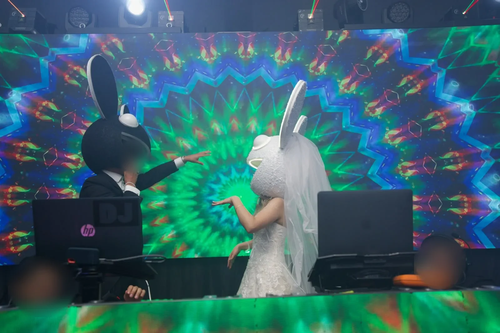 Los novios con cabezas LED frente a una pantalla de luces